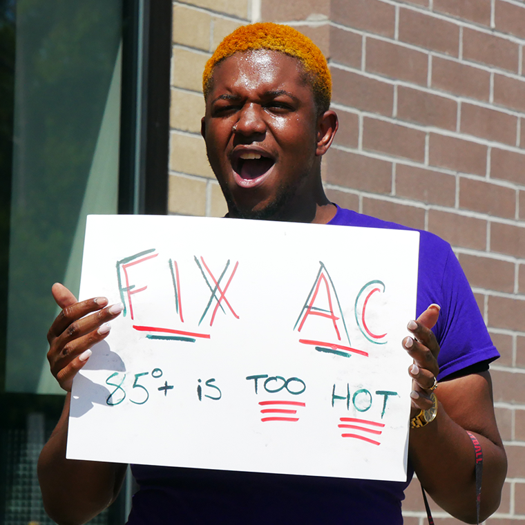 A young Black person yelling holds a sign that reads 